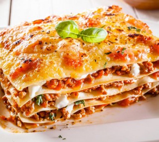 Portion of traditional durum wheat lasagne with bolognaise sauce, beef mince and cheese in alternating layers on a white plate